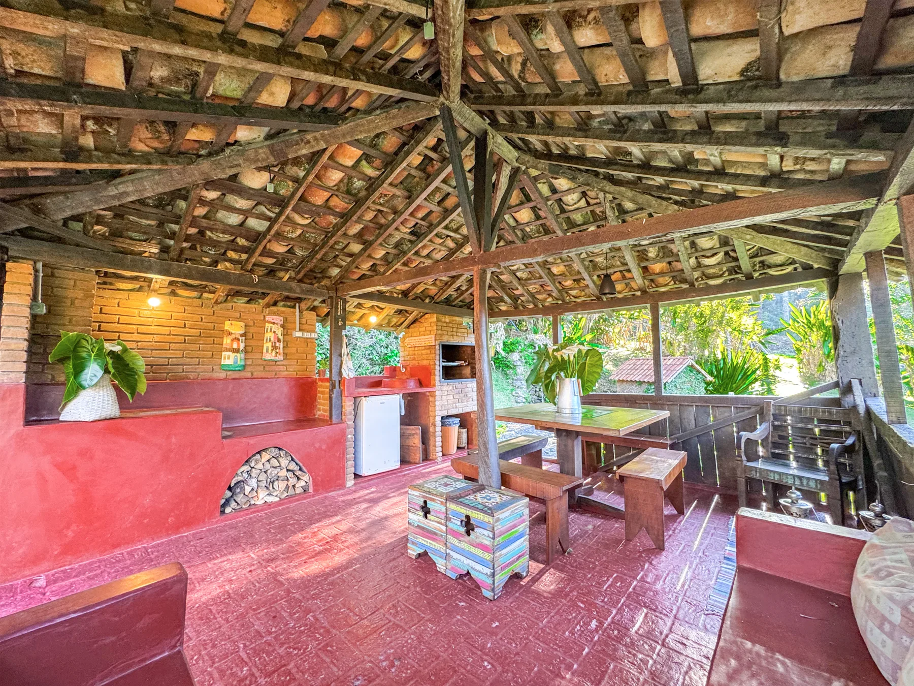 Vista ampla da área de churrasco, com bancos e mesas de madeira