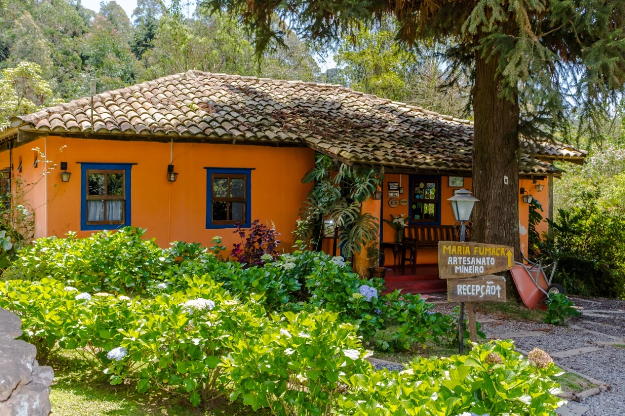 Jardins floridos e árvores ao redor do casarão da Pousada Trem das Cores